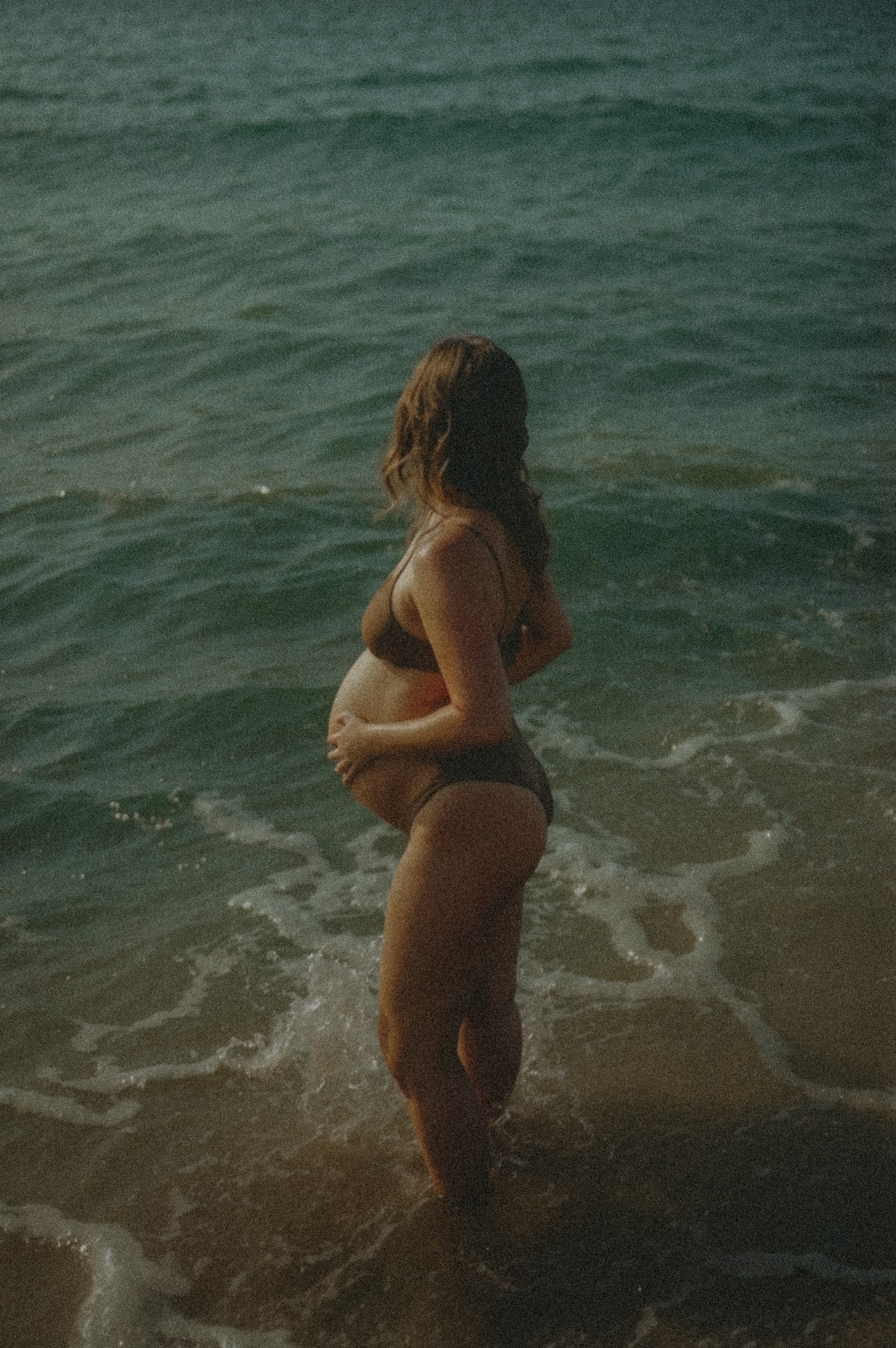 Woman standing in ocean waves at golden hour
