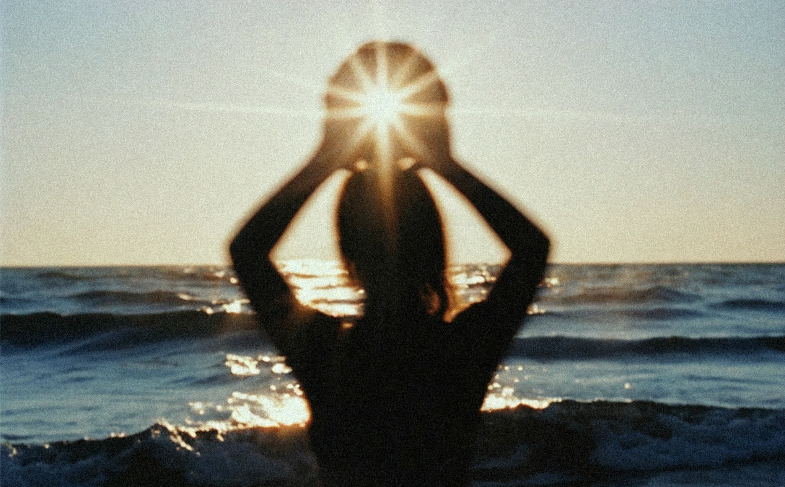 Woman silhouette at sunset in ocean with arms raised